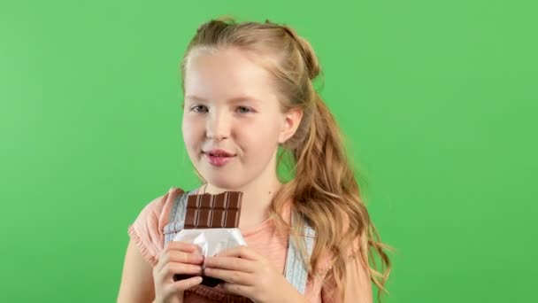 Van dichtbij gezien eet een grappig meisje een reep chocolade. Bruine lippen en tanden. Het kind likt zijn lippen — Stockvideo