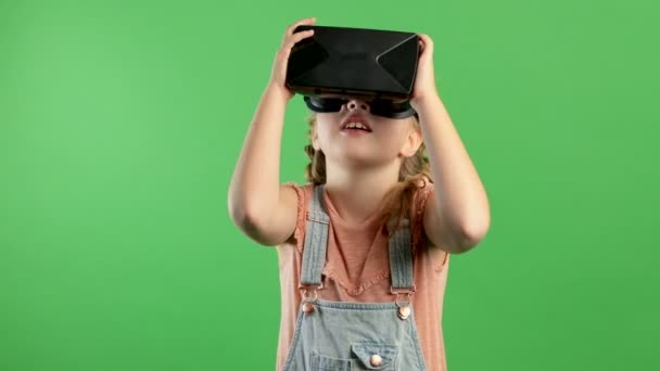 Αργή κίνηση χαμογελαστό κοριτσάκι που διασκεδάζει χρησιμοποιώντας γυαλιά VR, κορίτσι στέκεται σε απομονωμένο πράσινο φόντο. Έννοια της καινοτομίας, της τεχνολογίας, της οικογενειακής διασκέδασης, παιχνίδια, επόμενη γενιά — Αρχείο Βίντεο