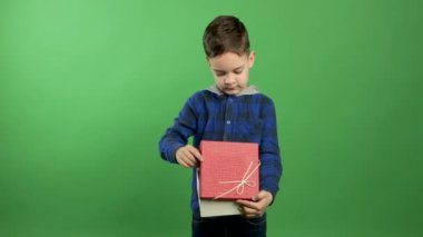 Şaşırmış çocuk yeşil bir arka planda sihirli bir hediyeyi açıyor ve dikizliyor.