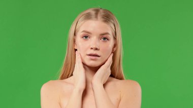 Nazik, güzel bir kız kameraya bakarak yanaklarını tutar. Etkileyici yüz ifadeleri. Kozmetik ve kaplıca