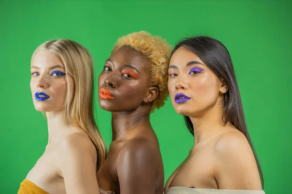 Tre unga leende kvinnor: flickor från Europa, Afrika-Amerika och Asien firar ungkarl med halvbakade axlar på en grön bakgrund. — Stockfoto