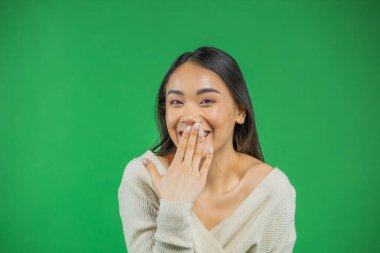 Gülümseyen Asyalı genç kadın ağzının yanında elini tutuyor kameraya bakıyor, başarı ve zafer kavramına bakıyor.