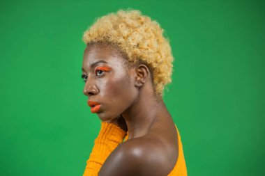 Yeşil arka planda, kısa kıvırcık saçlı, turuncu elbiseli, güzel Afrikalı kadın.