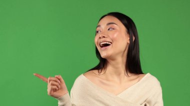 Güzel, çekici Asyalı genç kadınlar gülümseyerek kozmetik ürünler sergilemek için fotokopi alanını gösteriyorlar, yeşil arka planda izole edilmiş sağlıklı, temiz ve taze ciltli mutluluğu hissediyorlar, güzellik kavramı.