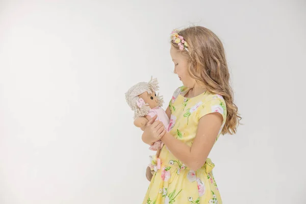 Uśmiechnięta dziewczyna trzyma lalkę i patrzy na nią w studio na odizolowanym tle — Zdjęcie stockowe