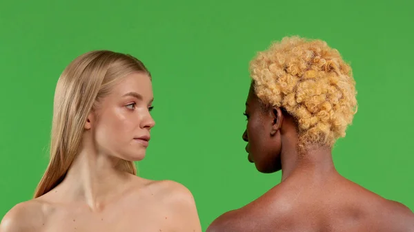 Portrait en gros plan de deux belles jeunes femmes blondes et à la peau foncée, une femme debout face à la caméra et l'autre dos à la caméra et se regardant — Photo