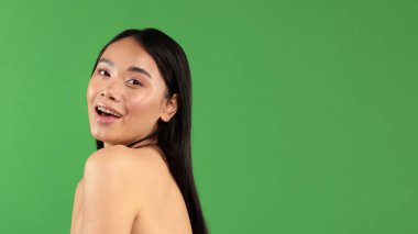 Güzellik kameraya bakıp güler ve gülümser. Yeşil arka planda izole edilmiş Asyalı genç beyaz modelin güzel portresi.