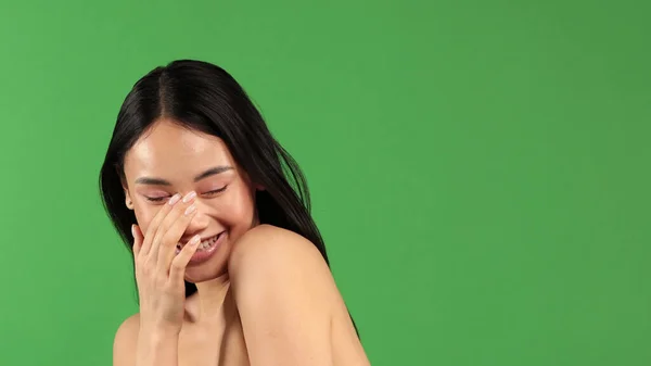 Glad förvånad upphetsad kvinna täcker sin mun med tom copyspace, närbild porträtt av vacker asiatisk kvinna, thai flicka, positiva mänskliga känslor ansiktsuttryck isolerad på grön bakgrund — Stockfoto