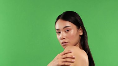 Güzel bir kadın portresi, yeşil arka planda güzellik, Asyalı bir kadın omzunu yarım yamalak kaldırıp kameraya bakıyor.