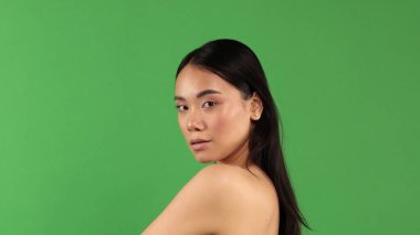 Yeşil arka planda genç Asyalı güzel bir kızın portresi. Omuzları kameraya dönük ve kameraya bakıyor.
