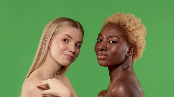Närbild skönhet porträtt av två olika nationer kvinnor, afrikanska amerikanska och asiatiska flickor med naturlig makeup poserar tillsammans vid kameran isolerad över grön bakgrund — Stockfoto