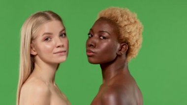 Çok kültürlü arkadaş kavramı. Yan yana duran çıplak omuzlu iki kadının portresi ve yarım yamalak kameraya bakan.