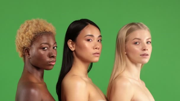 Closeup of beautiful young women of different races standing to each other in profile with a serious face and then simultaneously turning their heads and smiling at the camera. Portrait of three — Stock Video