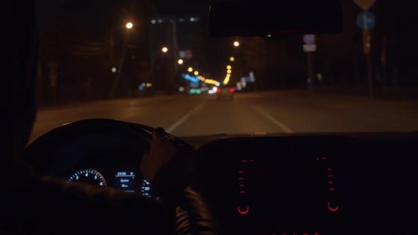 把人的手放在汽车的方向盘上 夜间驾驶时 控制台和仪表板在黑暗的车内点亮灯 Pov 城市街道上模糊不清的灯光 — 图库视频影像