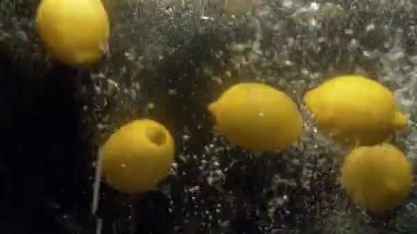 Закрыть Свежие Лимоны Падают Воду Всплеском Пузырьками Черном Фоне — стоковое видео