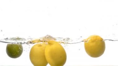 Suya düşen tatlı limonları büyük bir su sıçraması ve beyaz arka planda kabarcıklar ile kapatın. Yavaş çekim