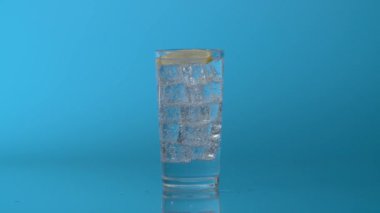 Bir dilim limonu mavi arka planda maden suyu ile bardağa düşür.