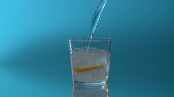 Fermer l'eau gazeuse minérale coulant dans un verre avec de la glace et une tranche de citron sur un fond bleu 