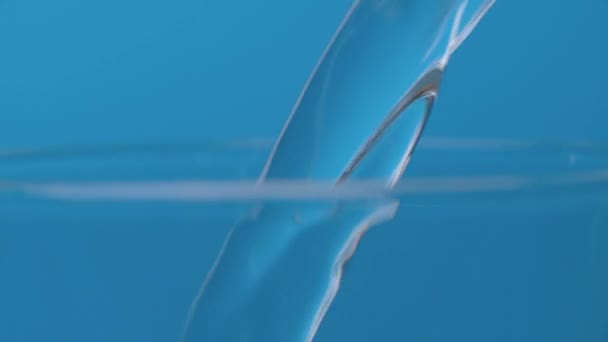 水ジェットがガラスに注ぐ 青を背景に炭酸ミネラルウォーターを極端にクローズアップ — ストック動画