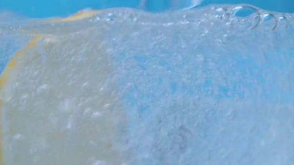 矿泉水倒入杯子里 极近的自然碳化矿泉水与冰和切片柠檬蓝色背景 冰上的气泡 — 图库视频影像