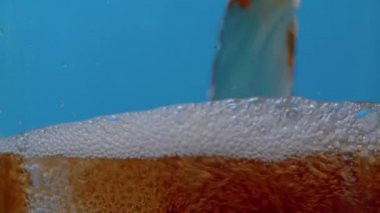Yakından bir bardağa karbonatlı içecek dolduruyorum. Kola köpüklü, buz küplü, şeffaf bardakta köpüklü, mavi arka planda. Coke Soda jeti yakın plan.