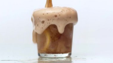 Buzlu ve dilimlenmiş limonlu bir bardağa kola dökülüyor. Bardakta köpük yükselir. Köpüklü içecek taşar ve masanın üzerine dökülür. Kapat, beyaz arkaplan, yavaş çekim