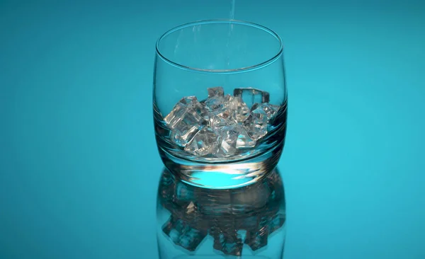 Água derramando em um copo com gelo — Fotografia de Stock