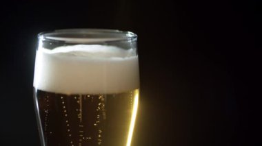 Birayı şeffaf camla kapat, düşük açılı kenar görüş, siyah arka plan. Bira köpüklü, kabarcıklar yüzeye çıkıyor..