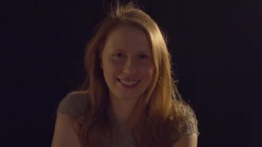 Close up portrait of a blond young smiling woman on a dark background. Pretty caucasian lady looking at camera. Blowing air, long hair