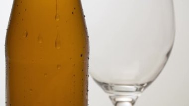 Masanın üzerindeki sisli soğuk bira şişesini kapat. Arkasında şarap kadehi var. Beyaz arka planda makro çekim. Akan su damlaları. El yapımı bira yakın plan.