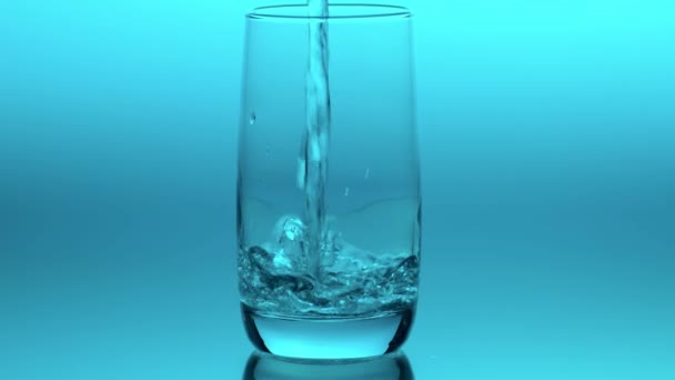 在蓝色背景上以慢动作将清澈清澈的水倒入透明的玻璃杯中 健康的生活方式概念 简单明了 — 图库视频影像