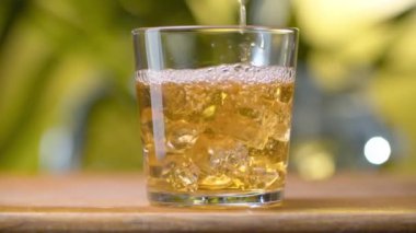 Sarı ışık şeffaf suyu bardağa dökülüyor. Doğal yeşil arka planda kabarcıklar var. Elmayı kapat, buzlu üzüm suyu. Sağlıklı yeme kavramı.