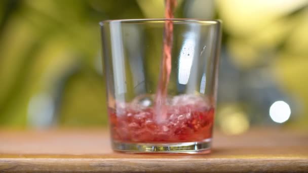 赤透明なジュースやワインをガラスに注ぎ 自然な緑の背景にスプラッシュや泡があります チェリーまたはザクロまたはクランベリージュースまたはワインを閉じます 健康的な食事のコンセプト — ストック動画