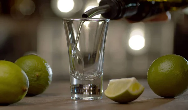 Barmene yakın bardağa tekila dolduruyor. Limonlar masada. Bulanık ampullerin arkaplanındaki çubuk sayacı.