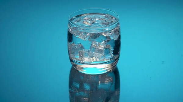Close up tonic, soda sparkling water in a glass with ice on a blue background. Refreshing mineral water.