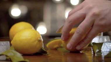 Erkek eli, arka plandaki bulanık ampullerin üzerine limonu sıkıştırıp masaya koyun. Tazeleyici içecekler pişiriyorum. Barmen yakın planda çalışıyor.