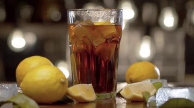 Erkek eli masaya bir bardak koyuyor. Long Island 'da buzlu çay ya da kola, buz, limon ve yapraklarla kaplı bir bardak bulanık ışık arka planında. Bar tezgahı yakın plan
