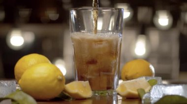 Cama dökülen kolayı kapat. Buzlu kola ve cam kaplı limon. Arka planda bulanık ışıklar. Limonlar ve yapraklar masada. Bardaktan gaz fışkırıyor, damlacıklar arka planda açıkça görülüyor..