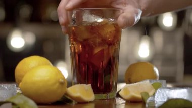 Erkek eli masaya bir bardak koyuyor. Long Island 'da buzlu çay ya da kola, buz, limon ve yapraklarla kaplı bir bardak bulanık ışık arka planında. Bar tezgahı yakın plan