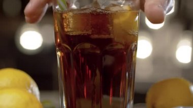 Barmen elini masaya kokteyl koyarak kapat. Long Island 'da buzlu çay ya da kola, buz, limon ve yapraklarla kaplı bir bardak bulanık ışık arka planında. Bar tezgahı yakın plan