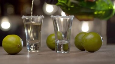 Barmene yakın bardaklara tekila dolduruyor ve güçlü bir alkollü içeceği ateşe veriyor. Bulanık ampullerin arkaplanındaki çubuk sayacı.