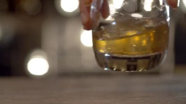 Barmenin elini kapat, bardakta buzla viski karıştır. Bulanık ampullerin arkaplanındaki çubuk sayacı.