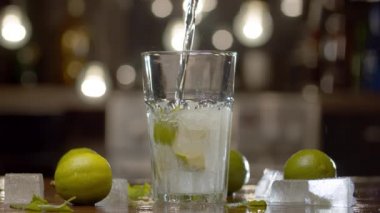 Kireç ve buzlu bir bardağa dökülen köpüklü suyu, arka planda bulanık ışıklarla kapatın. Tonik, soda ya da maden suyu. Gaz geliyor, atlayan su damlacıkları arka planda parlıyor