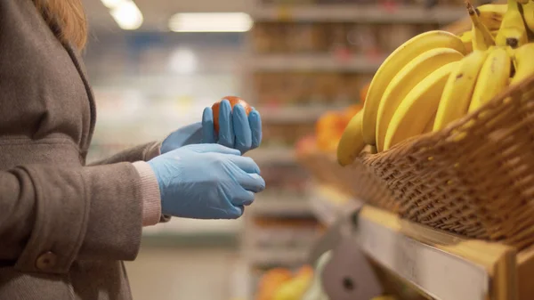 Süpermarkette portakal seçen mavi koruyucu eldivenli bir kadının elini kapat. Coronavirüs salgını