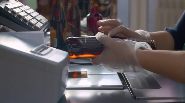 Close up checkout counter in the supermarket during coronavirus epidemic. Cashier\'s hands in protective gloves scans beer. COVID-19 pandemic