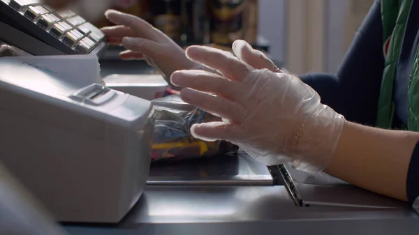 Close up checkout counter in the supermarket during coronavirus epidemic. Cashier's hands in protective gloves weighs goods. COVID-19 pandemic