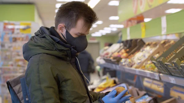 Koruyucu maskeli ve eldivenli bir adam süpermarkette kivi seçiyor. Şehirde koronavirüs salgını var. COVID-19 salgını
