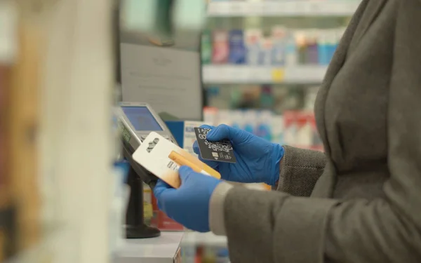 NFC teknoloji kredi kartı ödemesi. Temassız kredi kartıyla ödeme yapan koruyucu eldivenli bir kadın. Şehirde koronavirüs salgını.