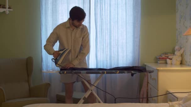 Άνδρας με σορτς και πουκάμισο σιδερώνει παντελόνια — Αρχείο Βίντεο