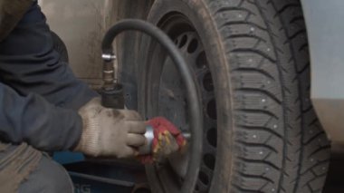 Otomatik ingiliz anahtarı kullanarak araba tekerleğindeki cıvataları bükerek işçinin ellerini kapat. Bir araç atölyesinde araba tekerleği değişiyor.